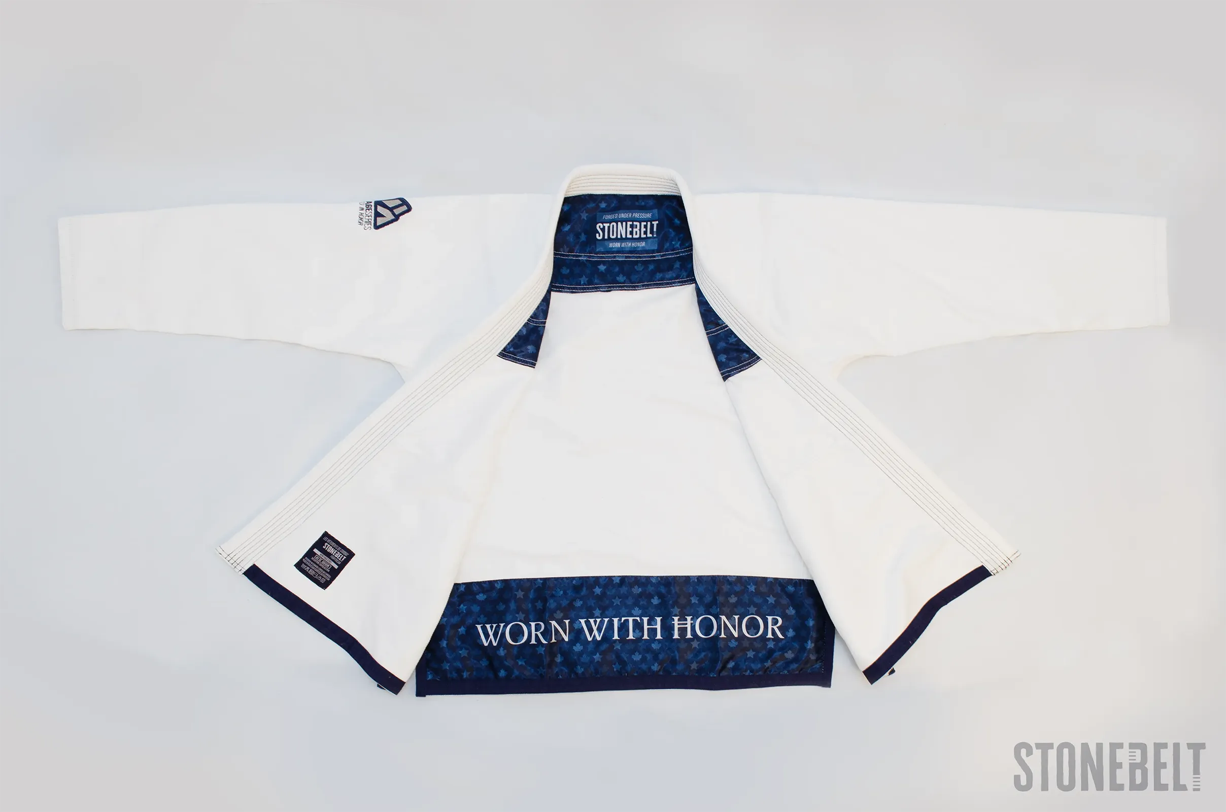 Full flat lay of Stonebelt Heritage BJJ gi jacket opened showing 450 GSM pearl weave construction, navy maple leaf interior lining with Worn With Honor panel, branded collar label, Heritage Series sleeve patch, care label, and navy contrast cuff trim