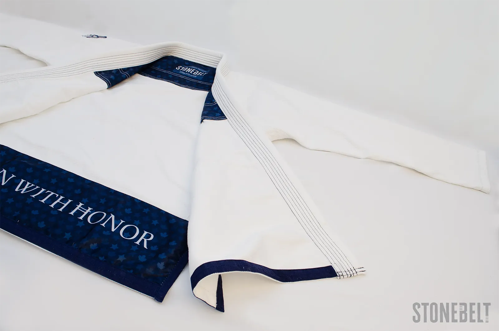 Stonebelt Heritage BJJ gi jacket laid open showing navy maple leaf interior lining with Worn With Honor text, Stonebelt neck label, multi-row lapel stitching, and navy sleeve cuff trim
