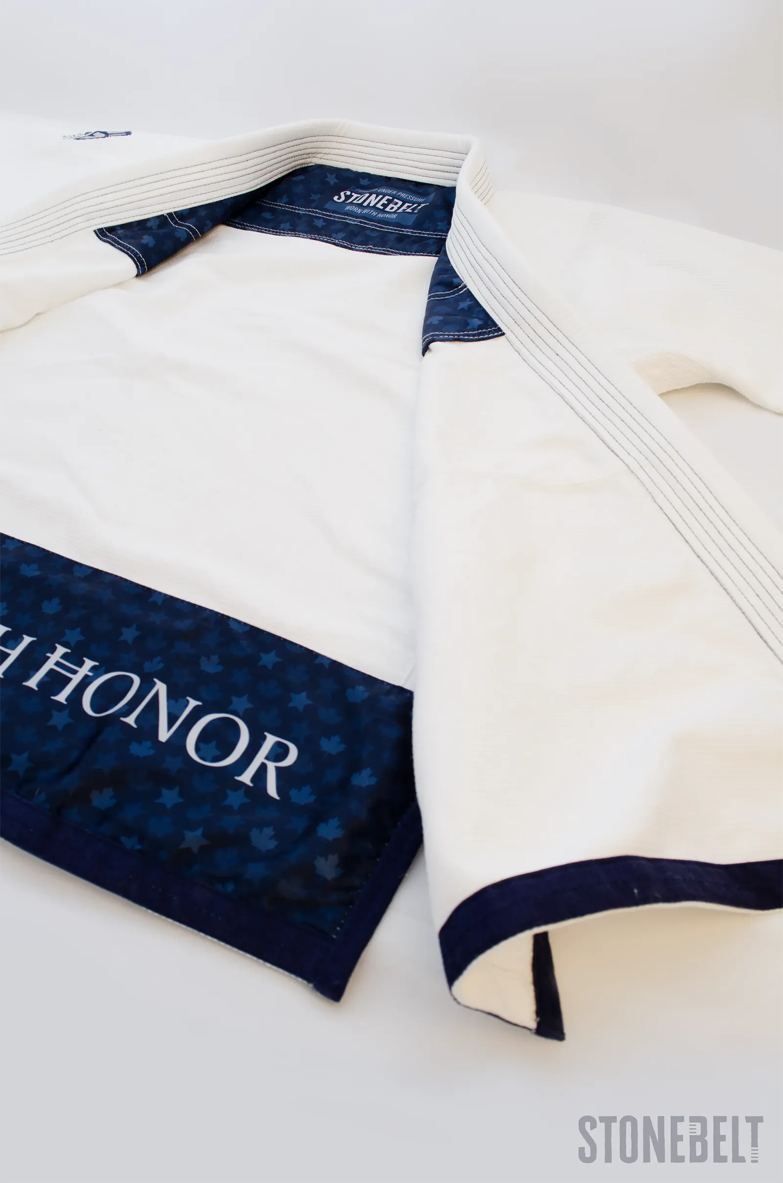 Interior of Stonebelt Heritage BJJ gi jacket showing navy blue maple leaf lining with Worn With Honor text, Stonebelt branded neck label, multi-row lapel stitching, and navy sleeve trim