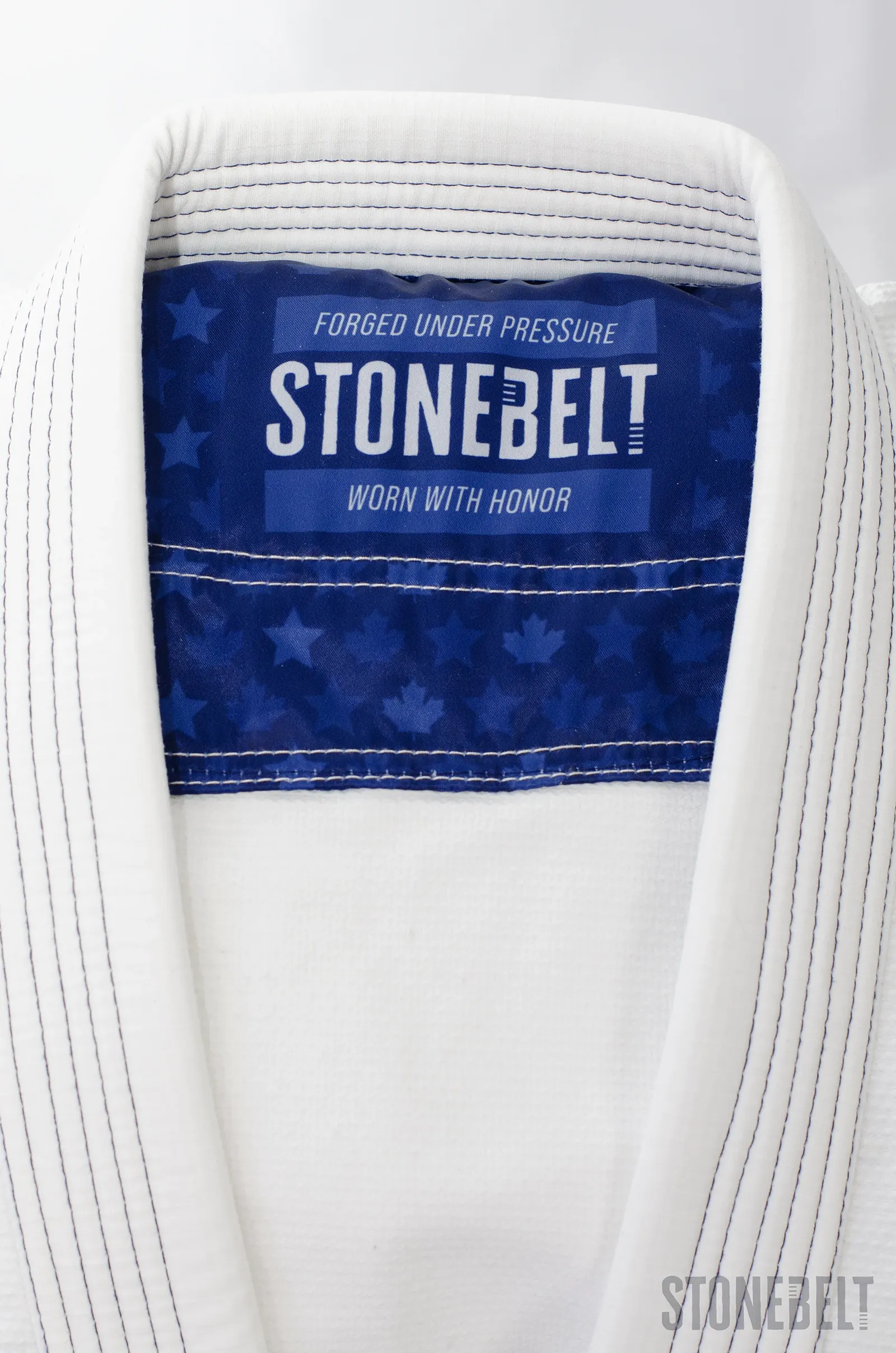 Interior collar of Stonebelt Heritage BJJ gi showing branded navy label with Forged Under Pressure and Worn With Honor text, maple leaf pattern lining, and reinforced multi-row lapel stitching