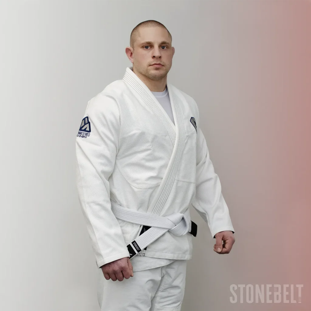 Practitioner wearing Stonebelt Heritage white BJJ gi front three-quarter view showing 450 GSM pearl weave jacket, navy embroidered chest logo, reinforced lapel, white belt, and ripstop pants