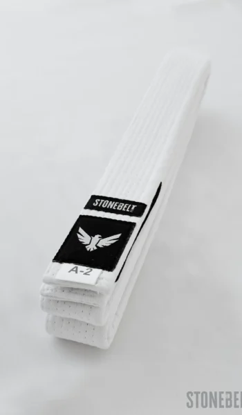 Close-up of folded Stonebelt BJJ white belt showing eagle logo patch, rank bar for stripe progression, and A-2 size label