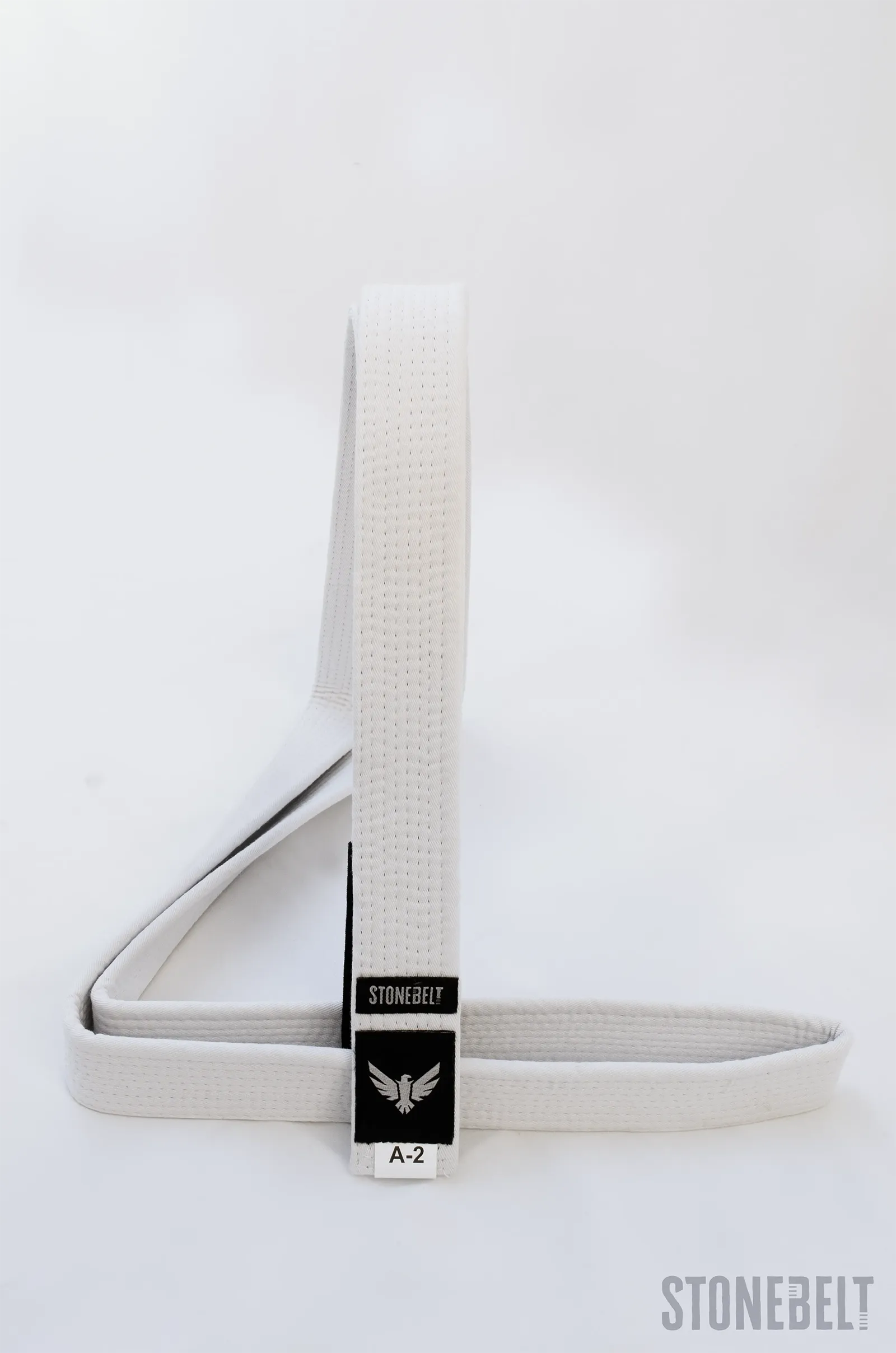 Stonebelt BJJ white belt arranged in a loop showing cotton construction, branded eagle patch, rank bar, and A-2 sizing