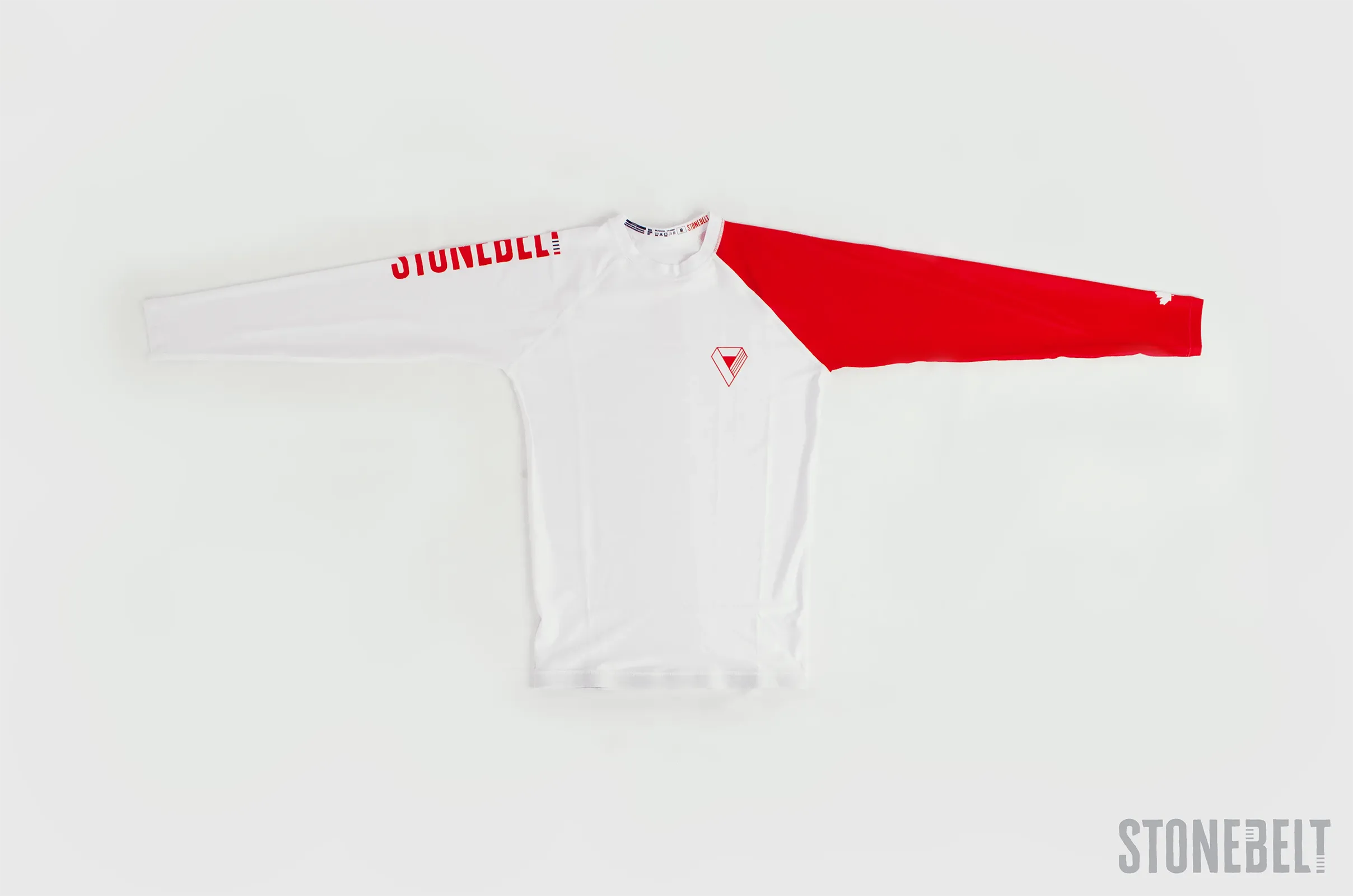 Front flat lay of Stonebelt Heritage long sleeve BJJ rashguard showing white body, red left sleeve, Stonebelt branding on right sleeve, and diamond chest logo