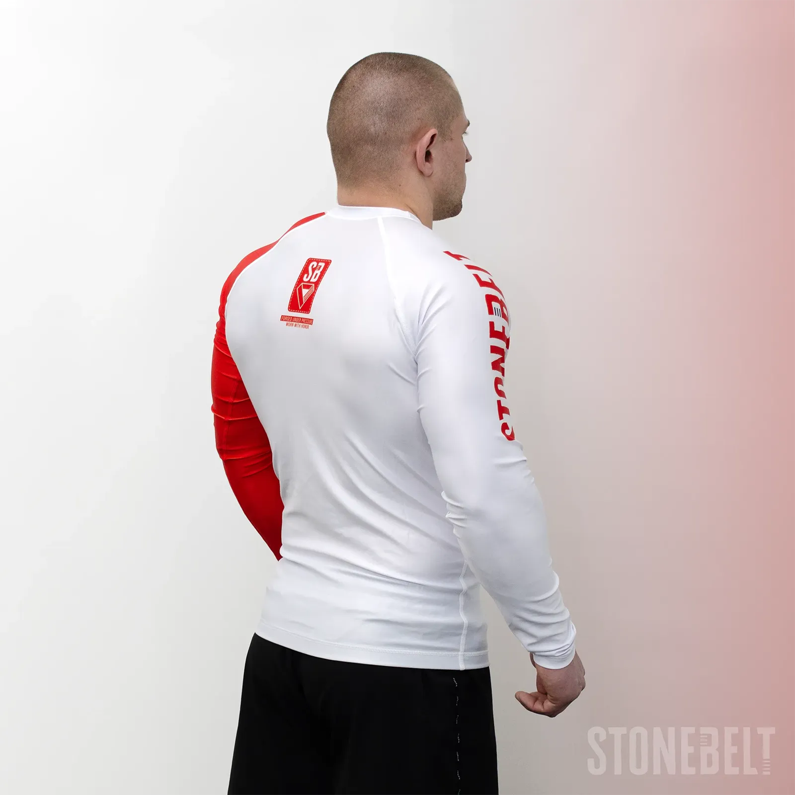 Rear angle of Stonebelt Heritage long sleeve rashguard showing SB back badge, red side panel, and Stonebelt arm text