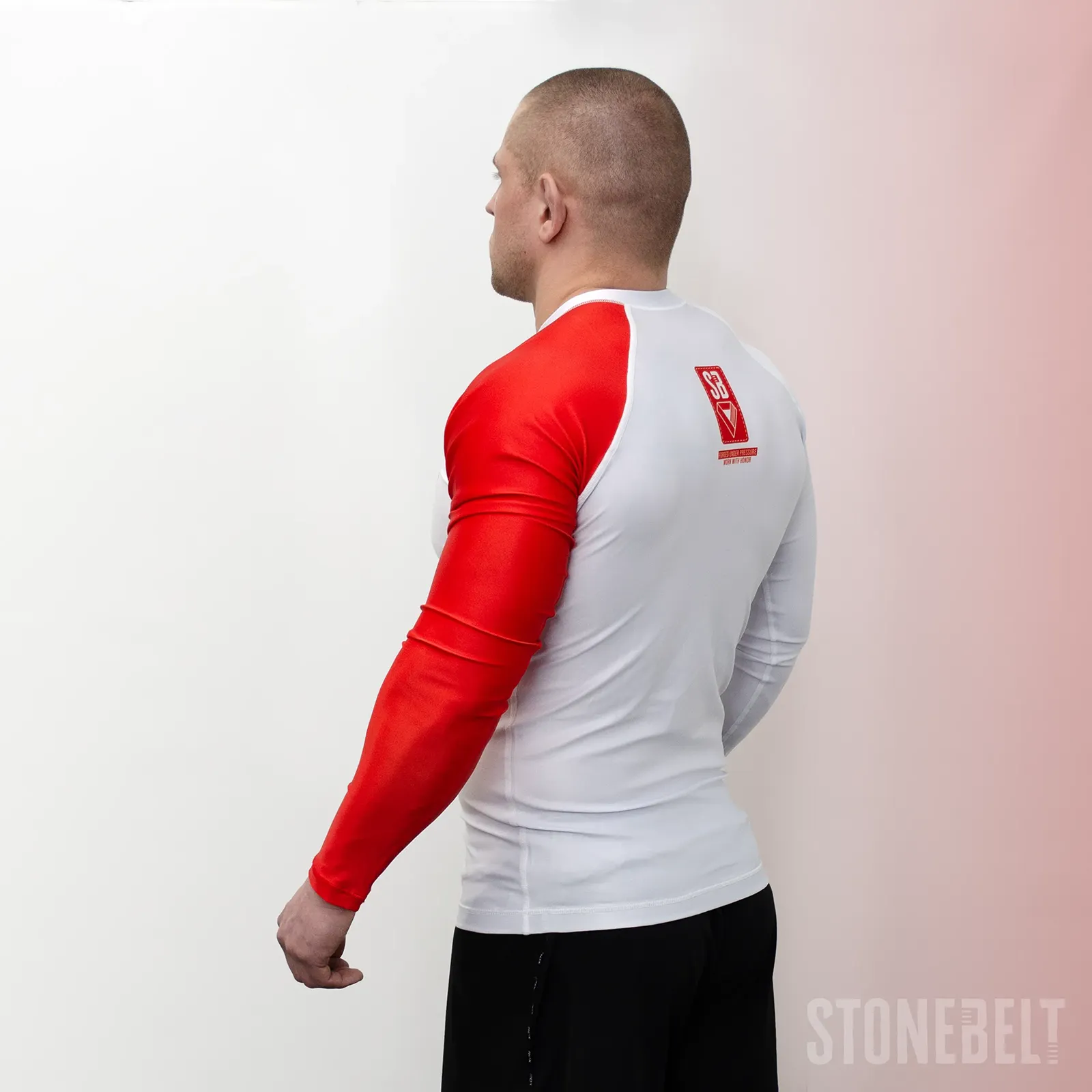 Rear left angle of Stonebelt Heritage long sleeve rashguard showing red sleeve, SB back badge, and raglan seam construction