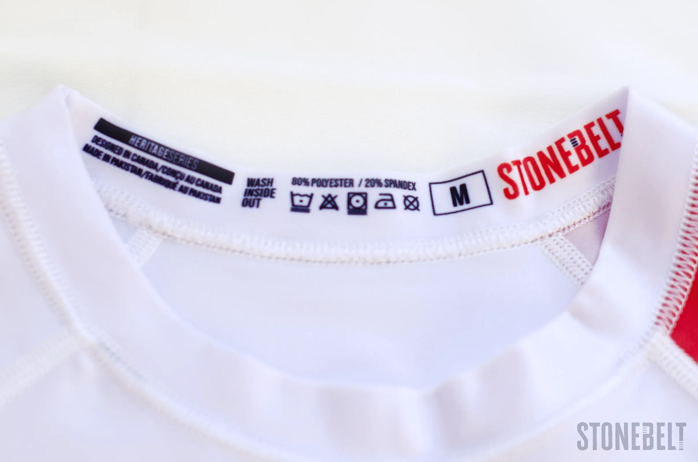 Close-up of Stonebelt Heritage rashguard neck label showing Heritage Series branding, 80% polyester 20% spandex composition, and care instructions