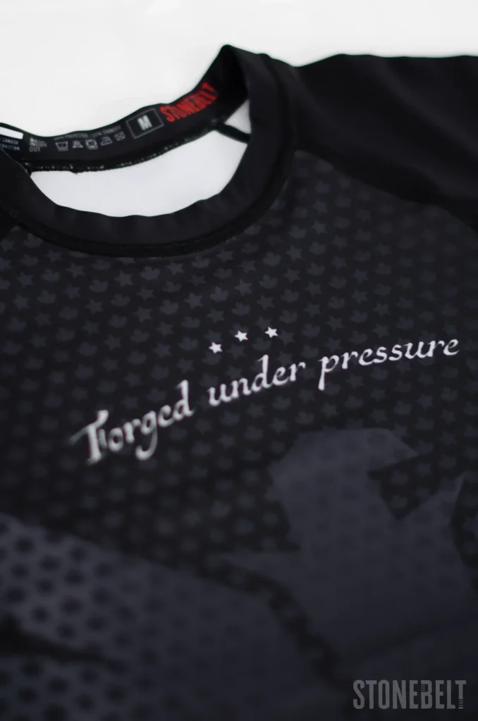 Close-up of Stonebelt Legion rashguard showing Forged Under Pressure sublimated text, maple leaf pattern, and branded neck label. No-Gi BJJ Sizing Guide