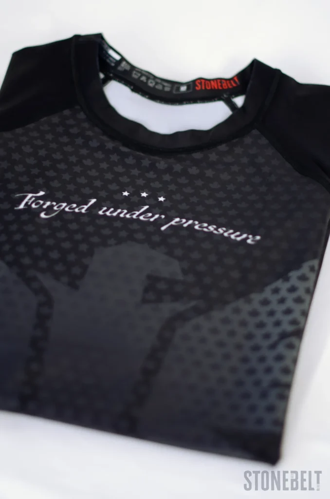 Flat lay of Stonebelt Legion short sleeve BJJ rashguard showing full front graphic with eagle design and maple leaf pattern