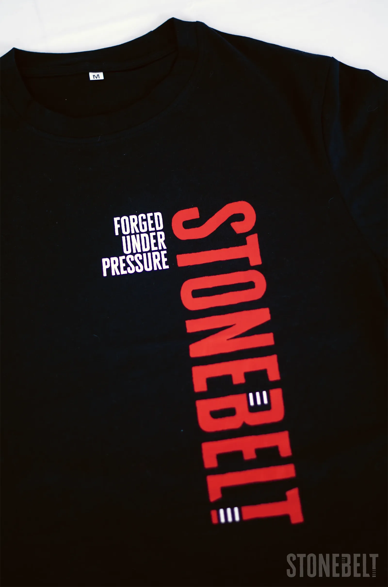 Flat lay of Stonebelt Classic Logo Tee in black showing Forged Under Pressure text and red vertical Stonebelt logo