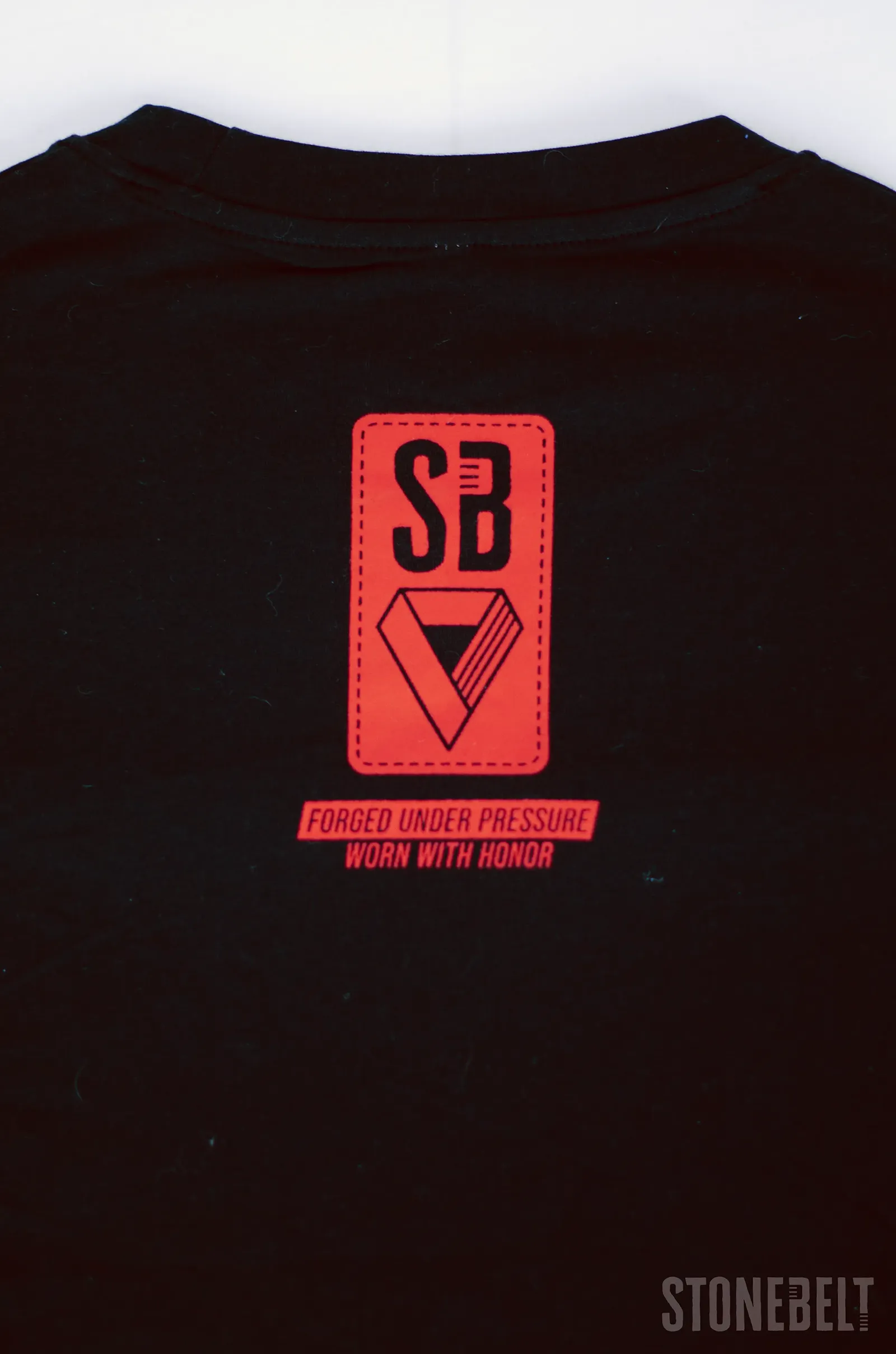 Flat lay detail of Stonebelt Classic Logo Tee black back showing red SB badge with Forged Under Pressure Worn With Honor print