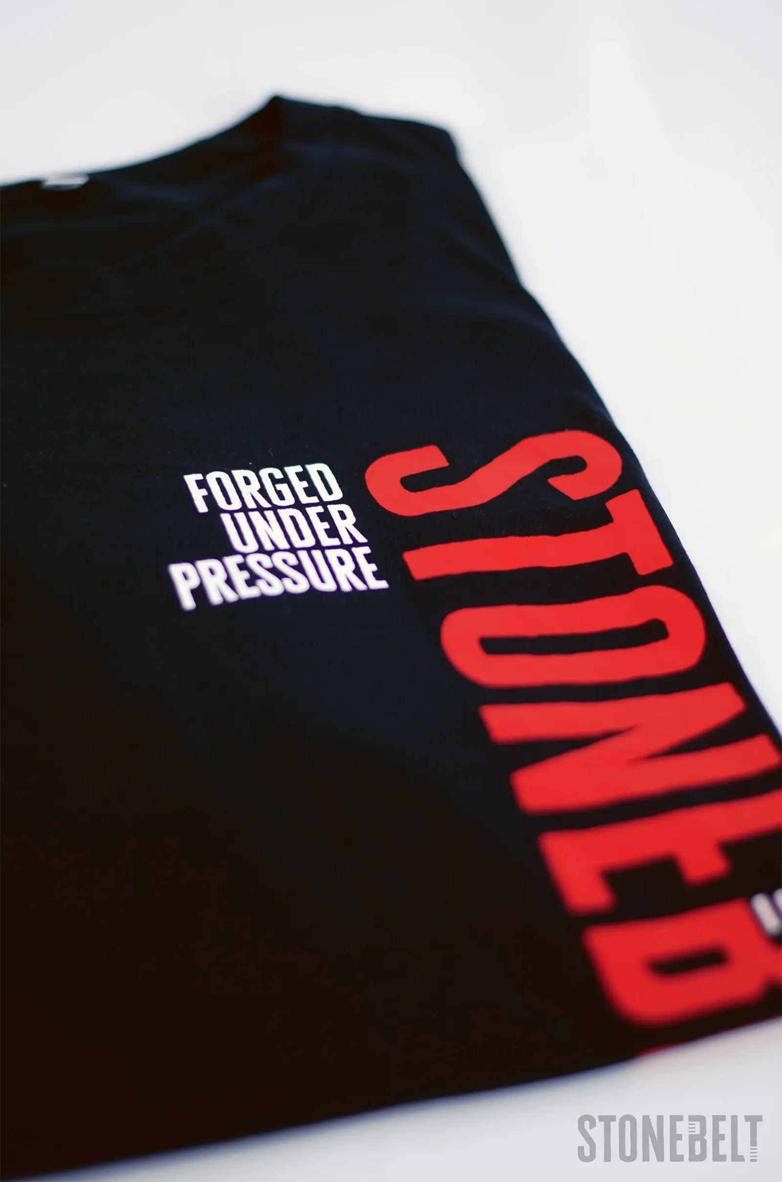 Close-up of Stonebelt Classic Logo Tee in black showing red Stonebelt vertical branding and white Forged Under Pressure text