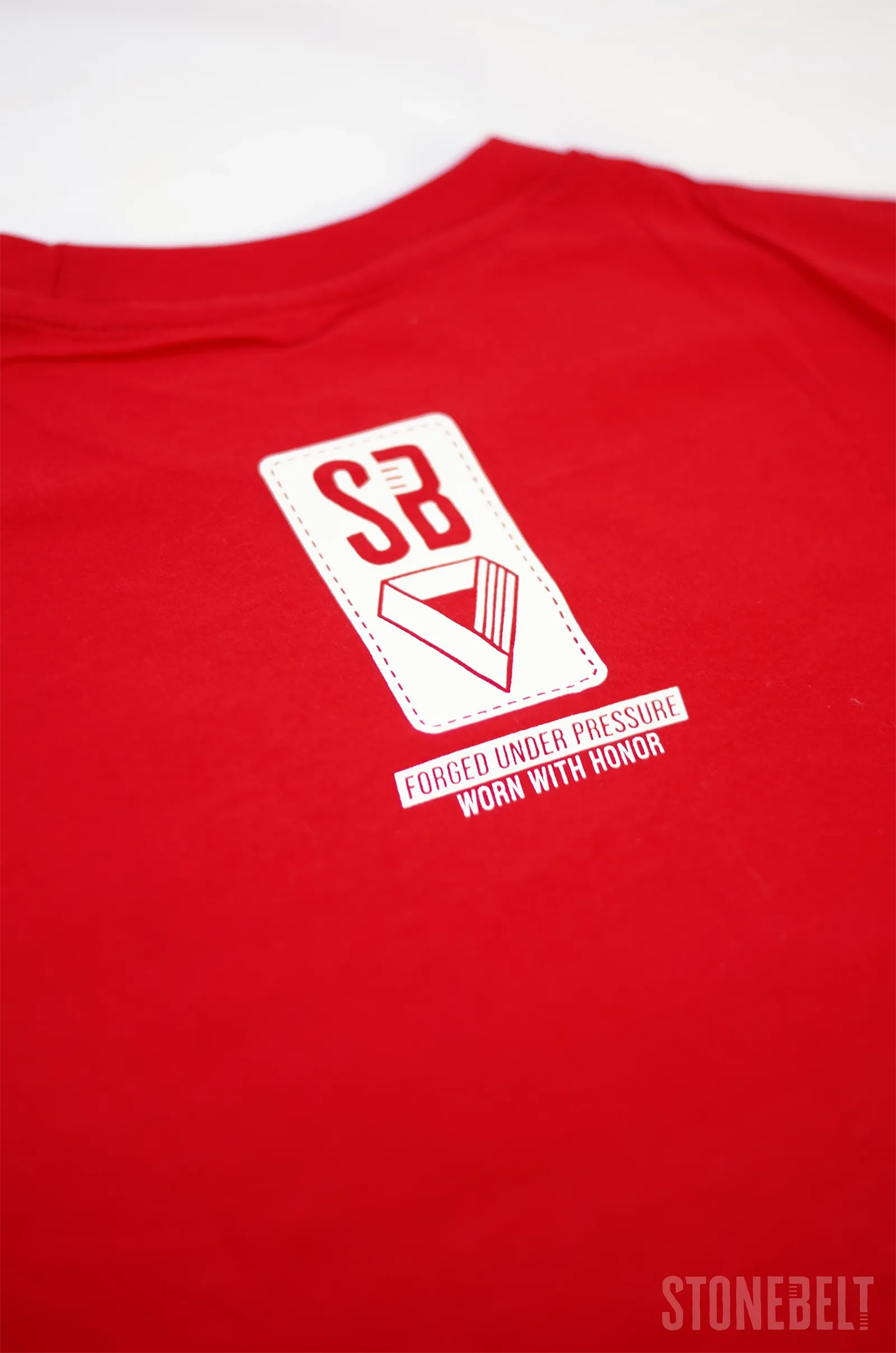 Flat lay detail of Stonebelt Classic Logo Tee red back showing SB badge and Forged Under Pressure Worn With Honor print.