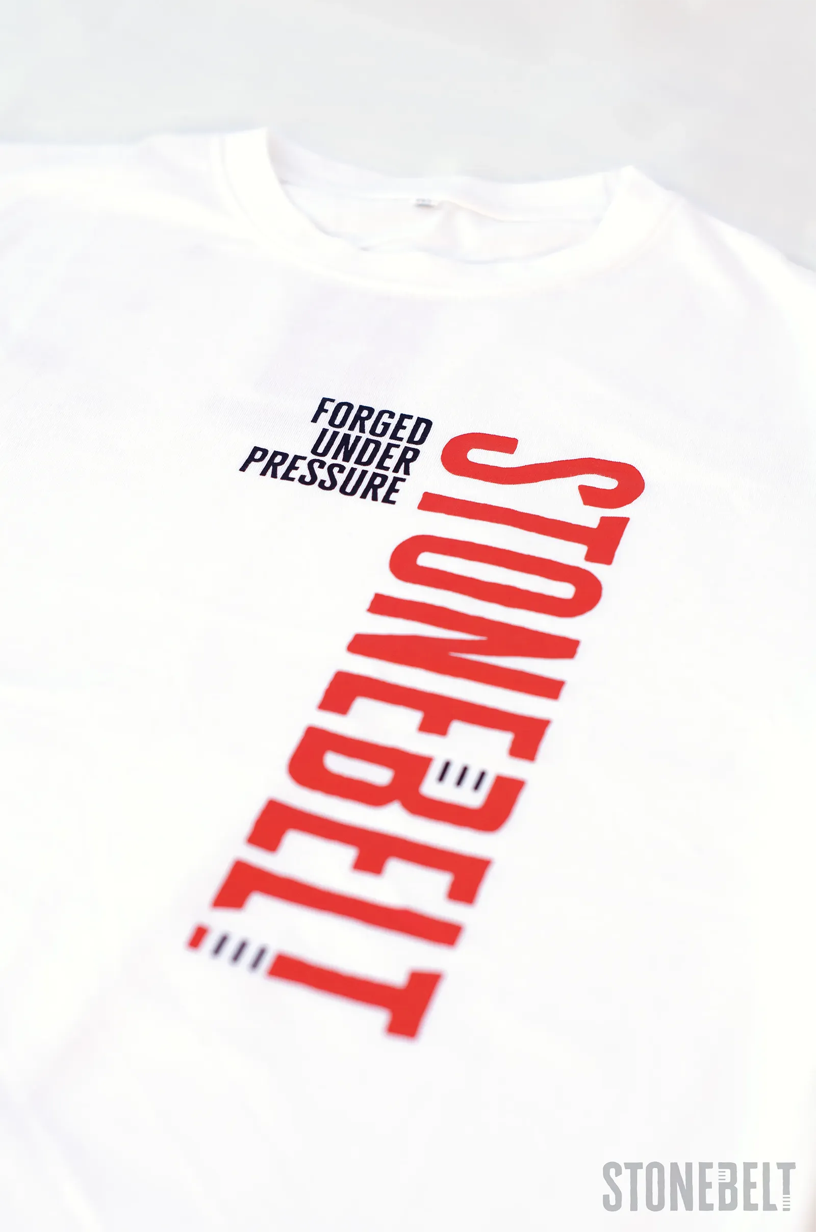 Flat lay of Stonebelt Classic Logo Tee in white showing red Stonebelt vertical branding and Forged Under Pressure text