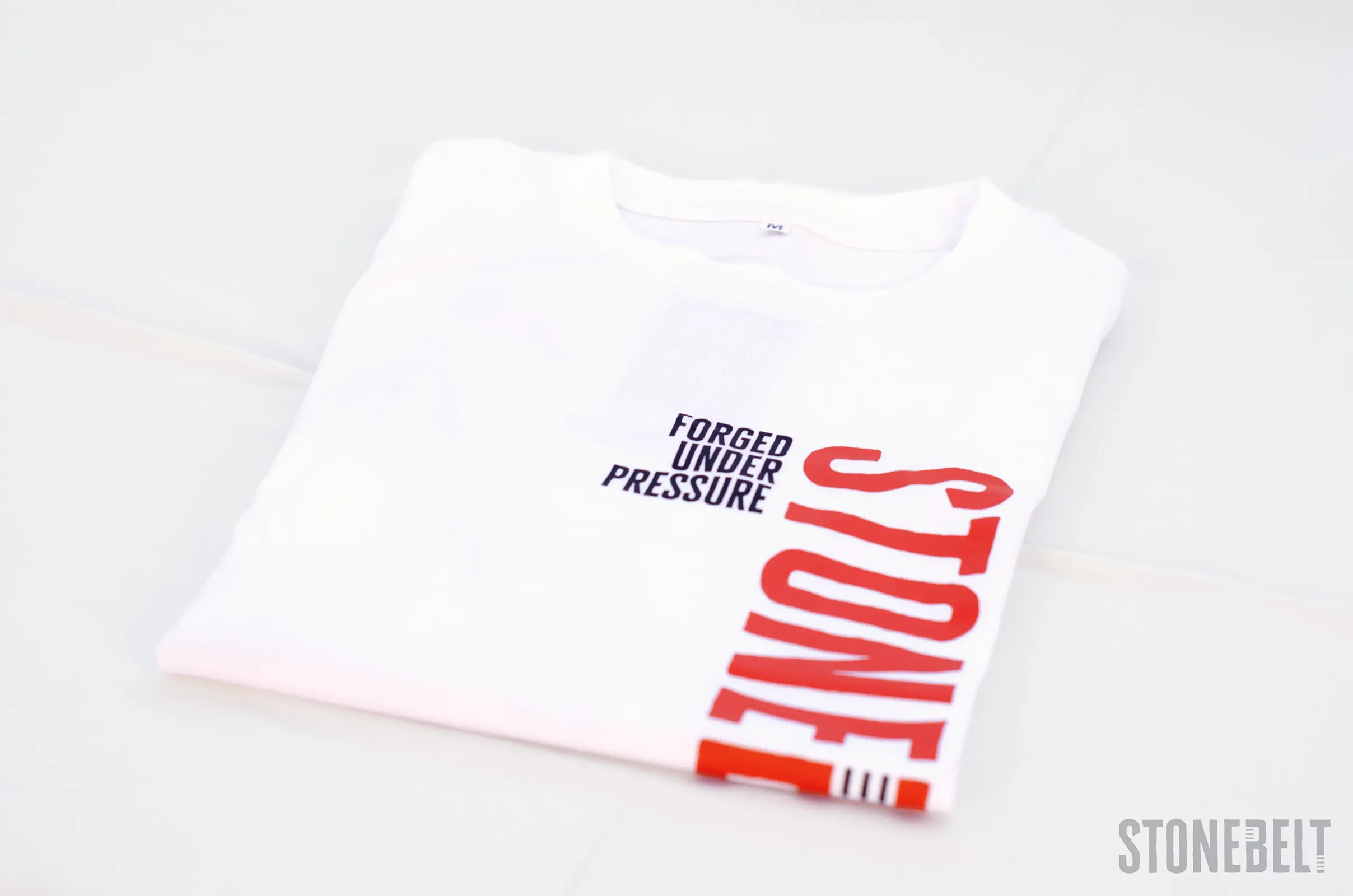 Folded Stonebelt Classic Logo Tee in white showing Forged Under Pressure text and partial Stonebelt vertical logo