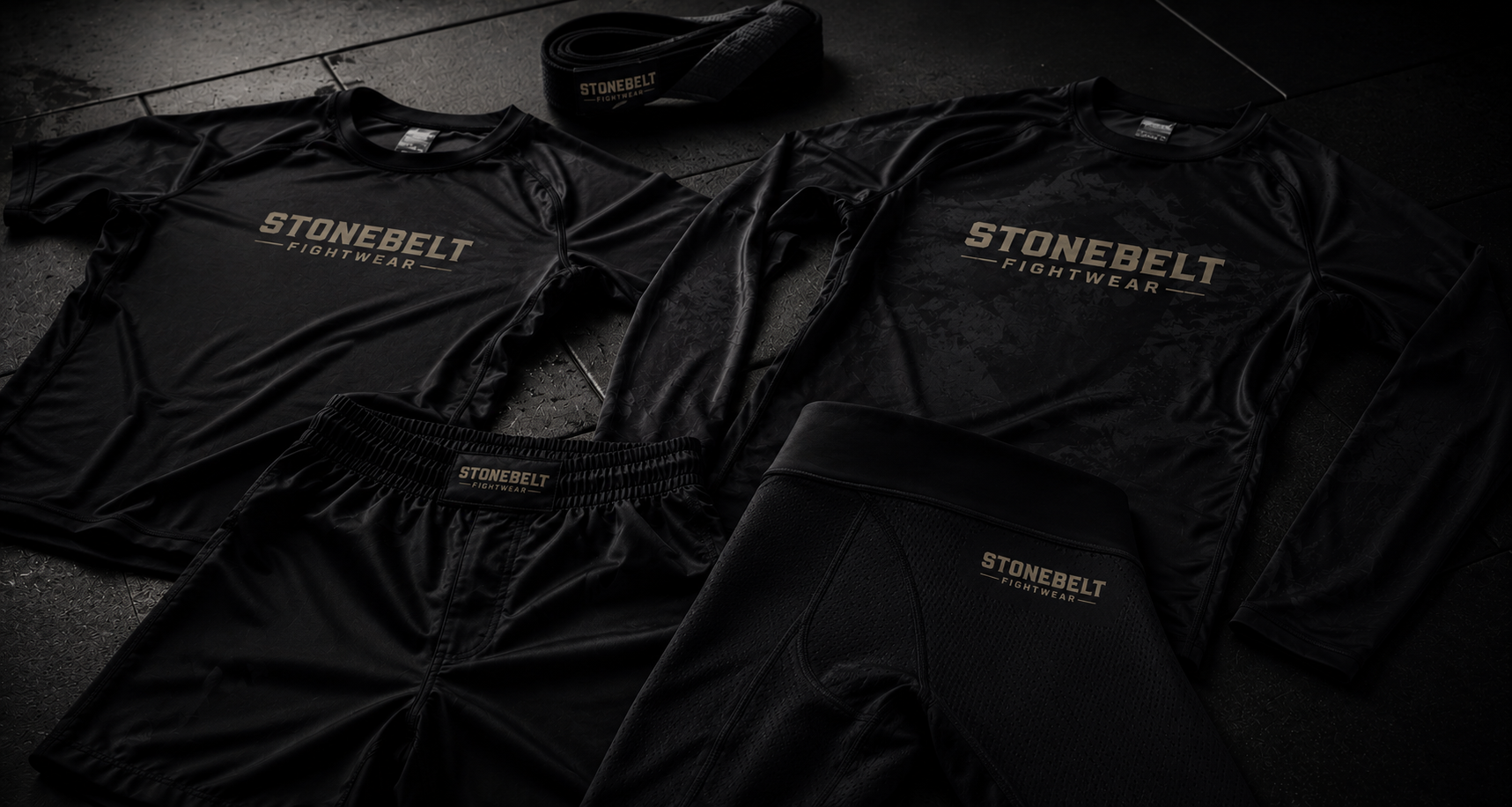 Stonebelt Fightwear no-gi BJJ gear laid out on gym floor, including rashguards, shorts, spats, and belt
