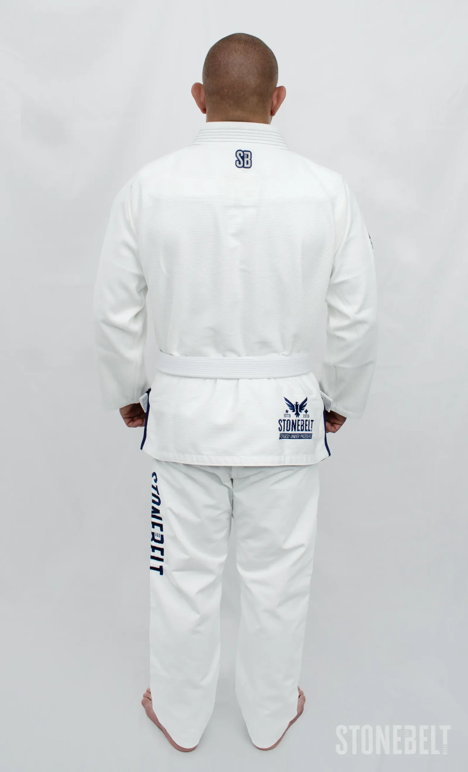 Stonebelt Heritage BJJ Gi in white, left side view on model, showing shoulder logo and Stonebelt pant embroidery