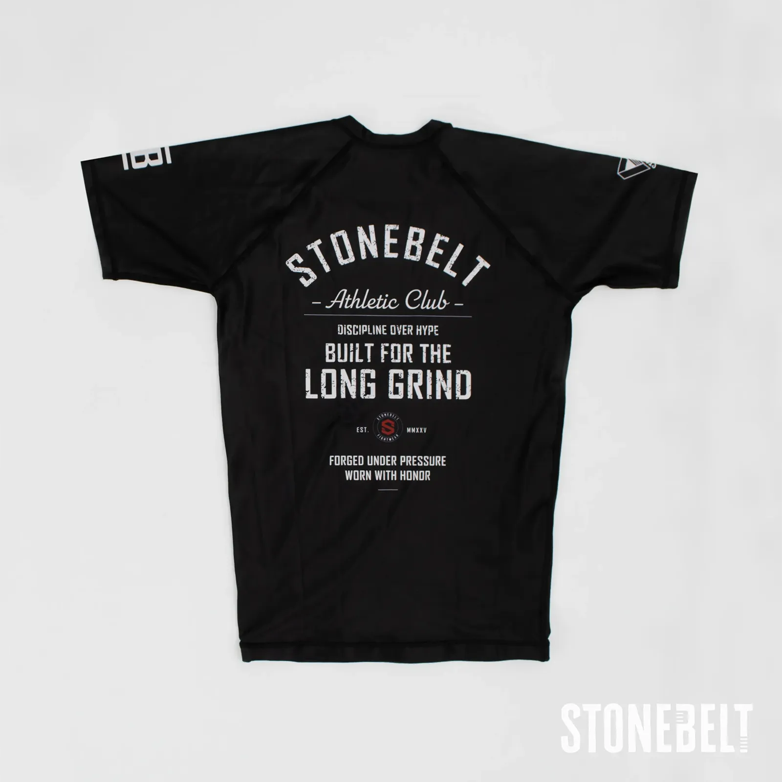 Stonebelt Athletic Club short sleeve BJJ rashguard in black, flat back view with Built for the Long Grind graphic