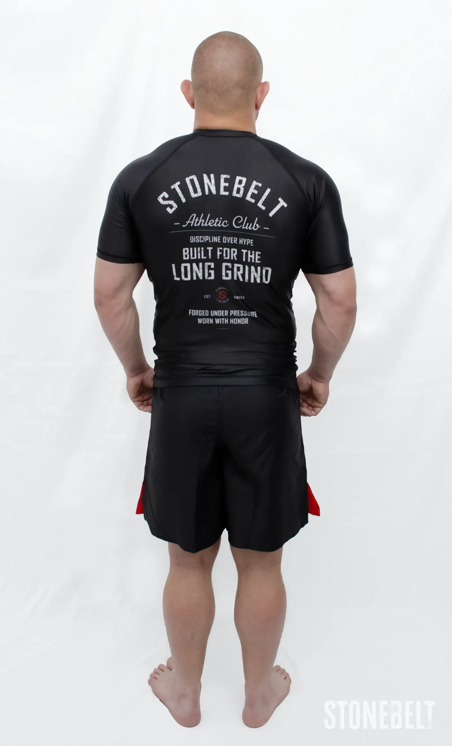 Model in Stonebelt Athletic Club black rashguard and black grappling shorts, back view with Built for the Long Grind graphic