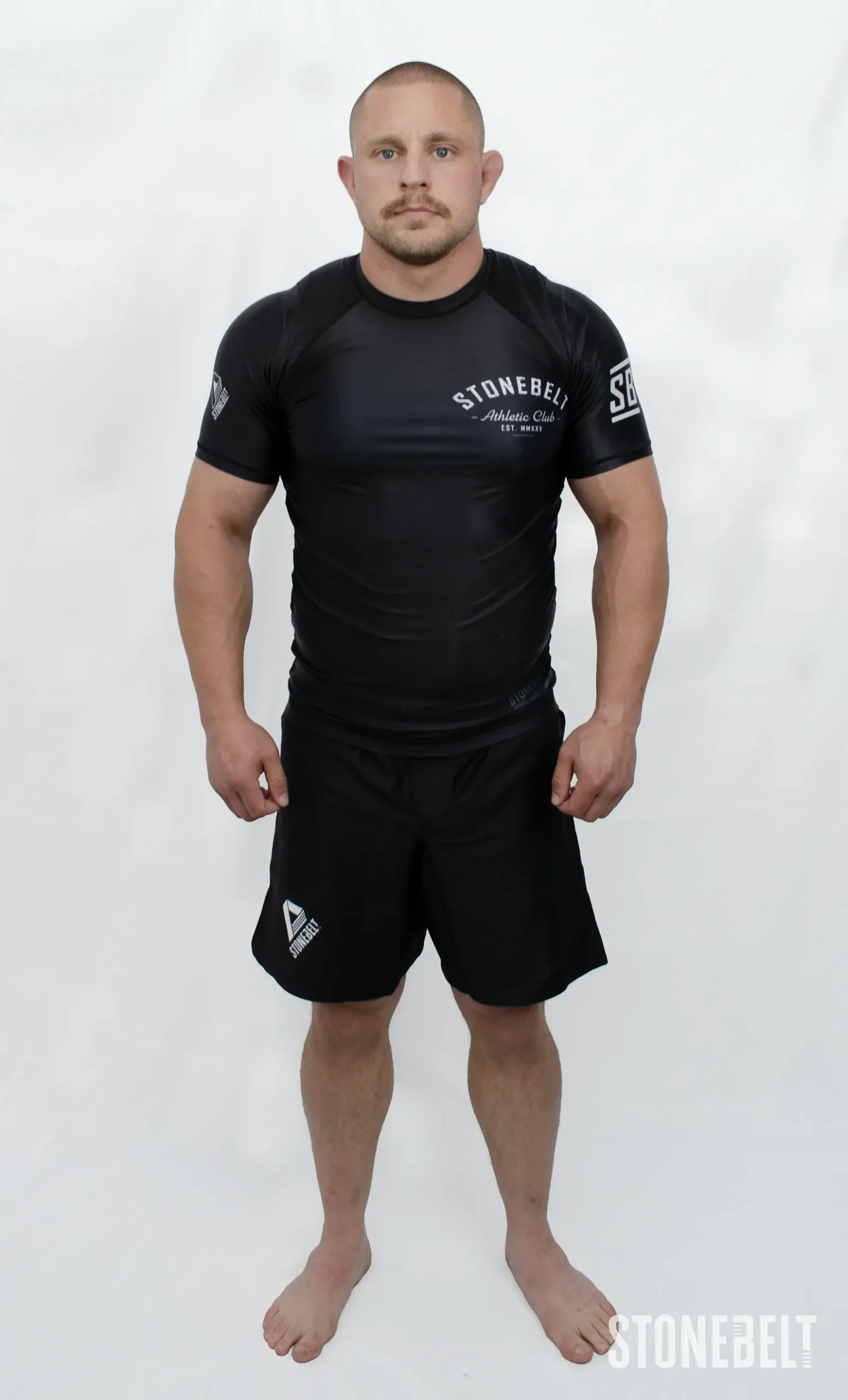 Model in Stonebelt Athletic Club black rashguard and black Heritage grappling shorts, front view