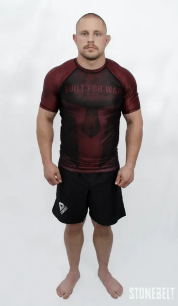 Model in Stonebelt Foundry red rashguard with Built for War graphic and black Heritage grappling shorts, front view