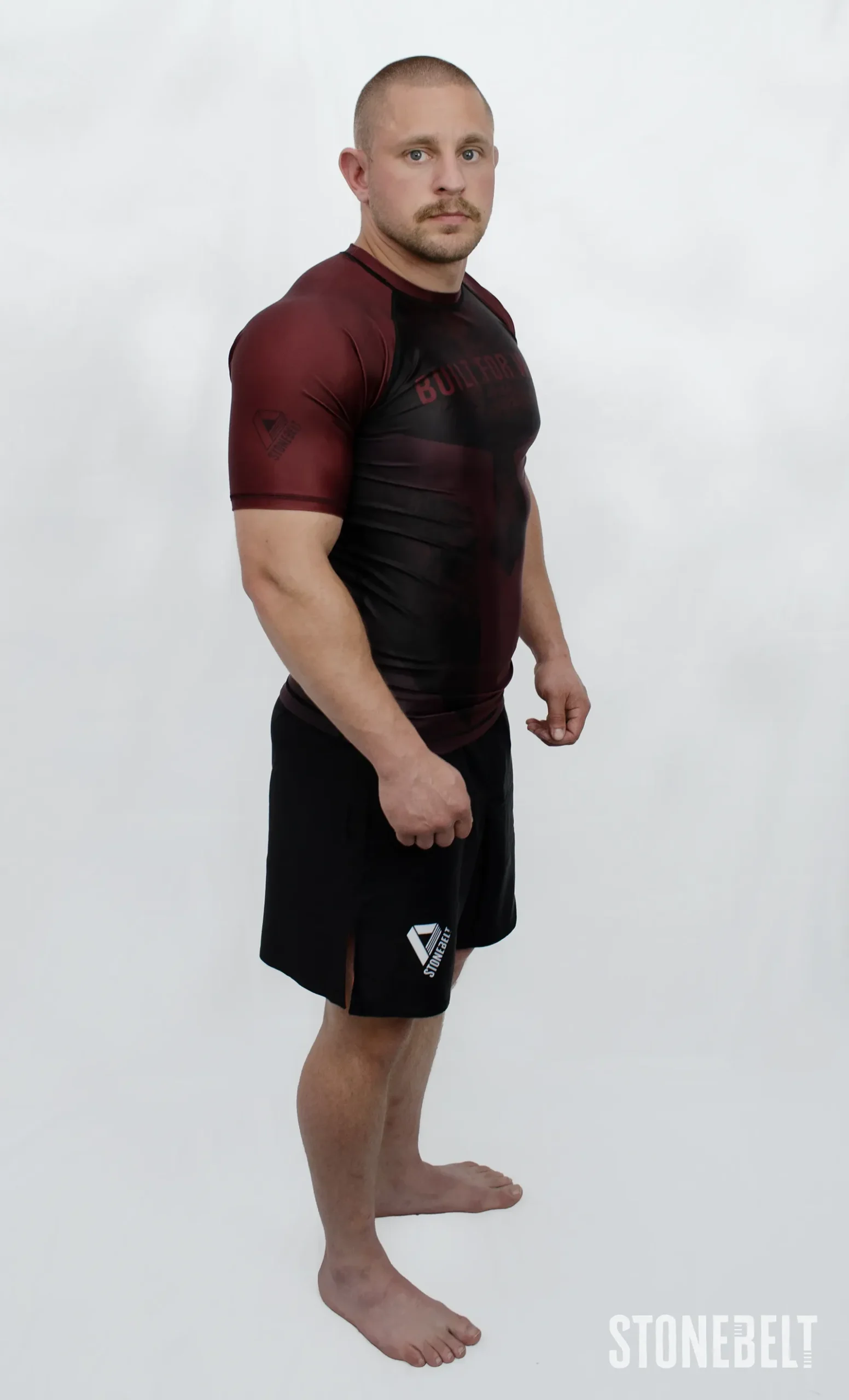 Model in Stonebelt Foundry red rashguard and black Heritage shorts, right side angled view with shoulder logo