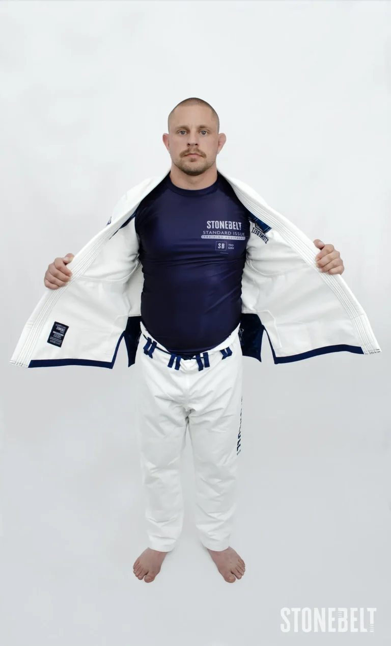 Model wearing Stonebelt Standard Issue navy rashguard under an open white Heritage BJJ gi jacket