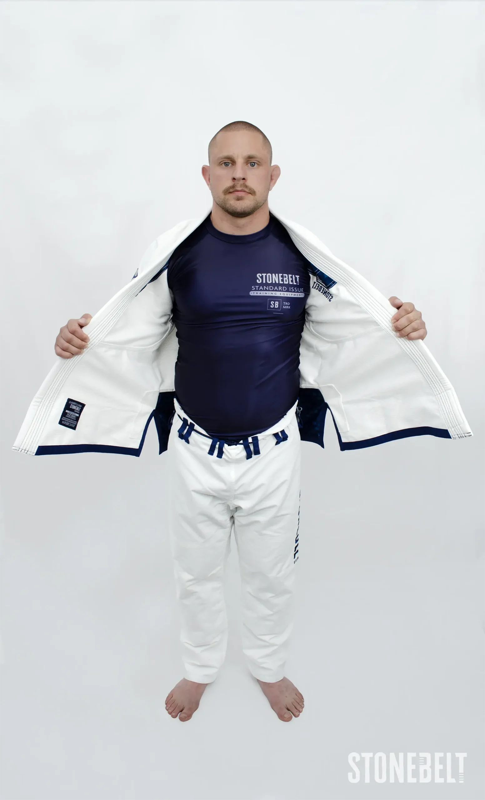 Model wearing Stonebelt Standard Issue navy rashguard under an open white Heritage BJJ gi jacket