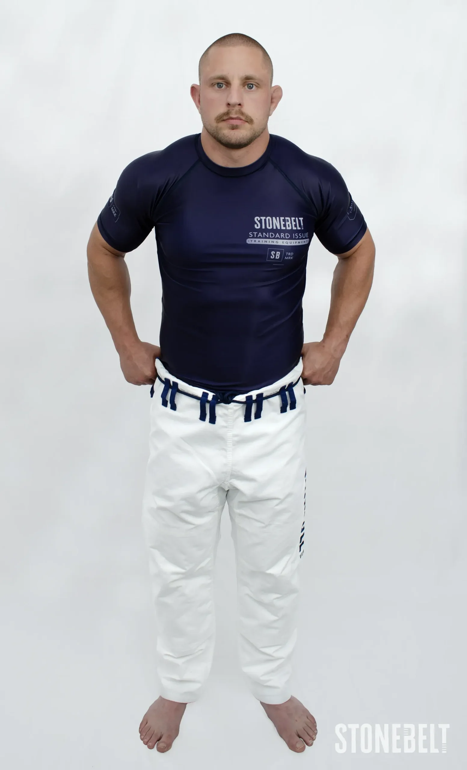 Model in Stonebelt Standard Issue navy rashguard and white Heritage gi pants, front view