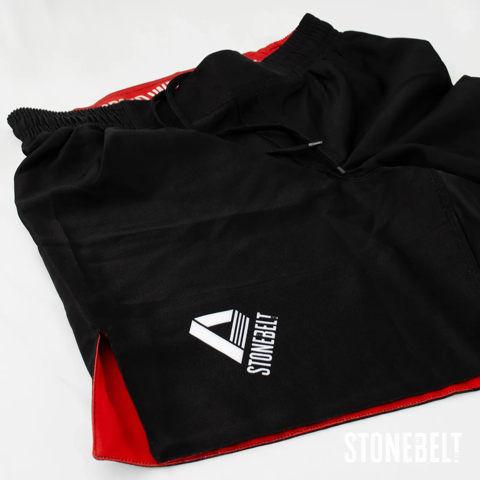 Angled detail of Stonebelt Heritage grappling shorts showing leg logo, side slit, and red inner lining